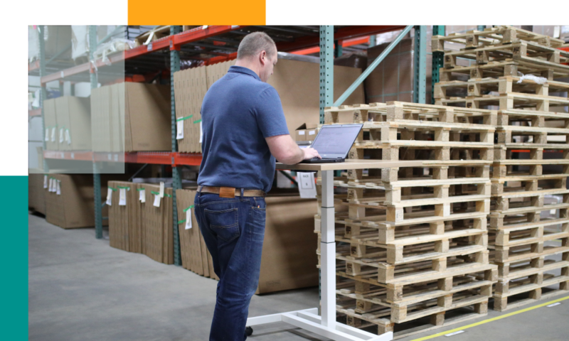 man standing at small desk looking at computer with flexible lease warehousing in background
